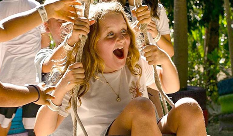 Child on swing laughing with excitement, surrounded by friends outdoors.