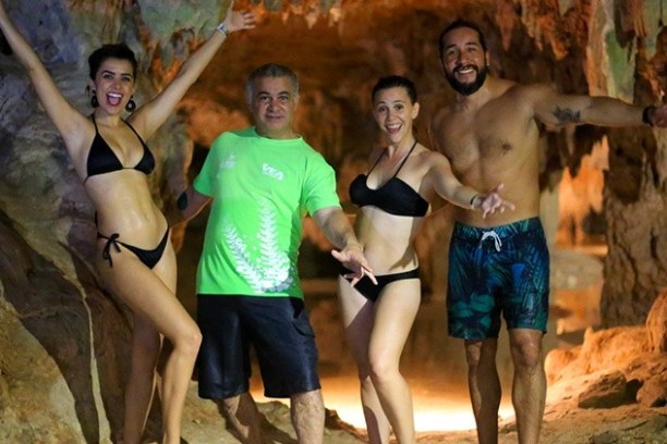 Four people in swimsuits posing inside a rocky cave, smiling and gesturing energetically.