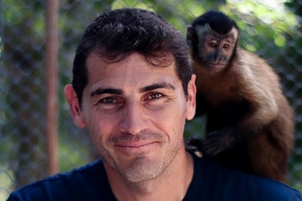 Man smiling with a monkey sitting on his shoulder, with a blurred outdoor background.
