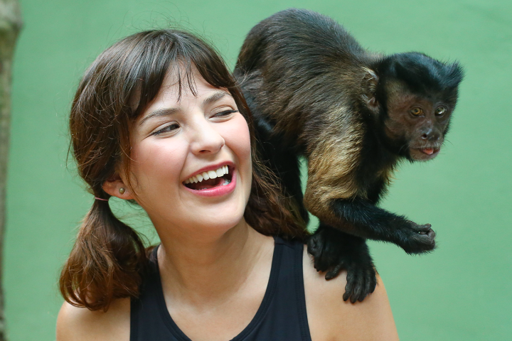 Smiling woman with a monkey on her shoulder against a green background.