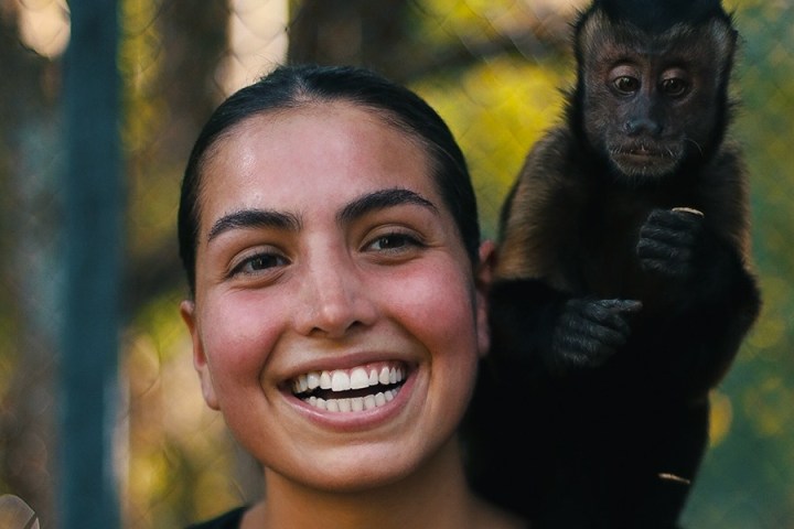 Smiling person with a monkey on their shoulder against a blurred nature background.