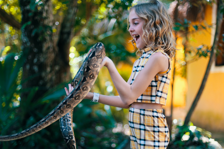 Child holding a large snake outdoors, both looking cheerful in a natural setting.