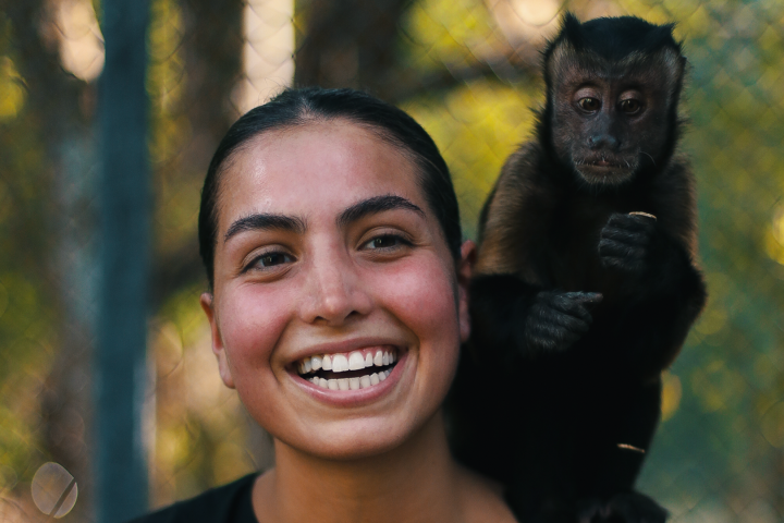 Smiling person with a small monkey on their shoulder, outdoors.