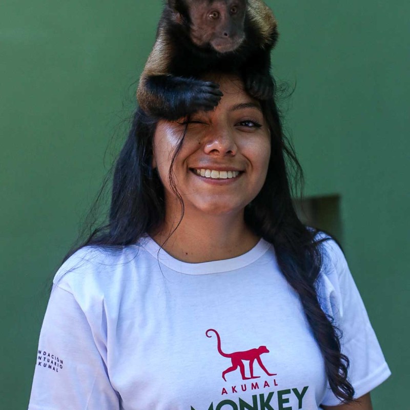 Woman smiling with a monkey on her head, wearing an Akumal Monkey Sanctuary T-shirt.