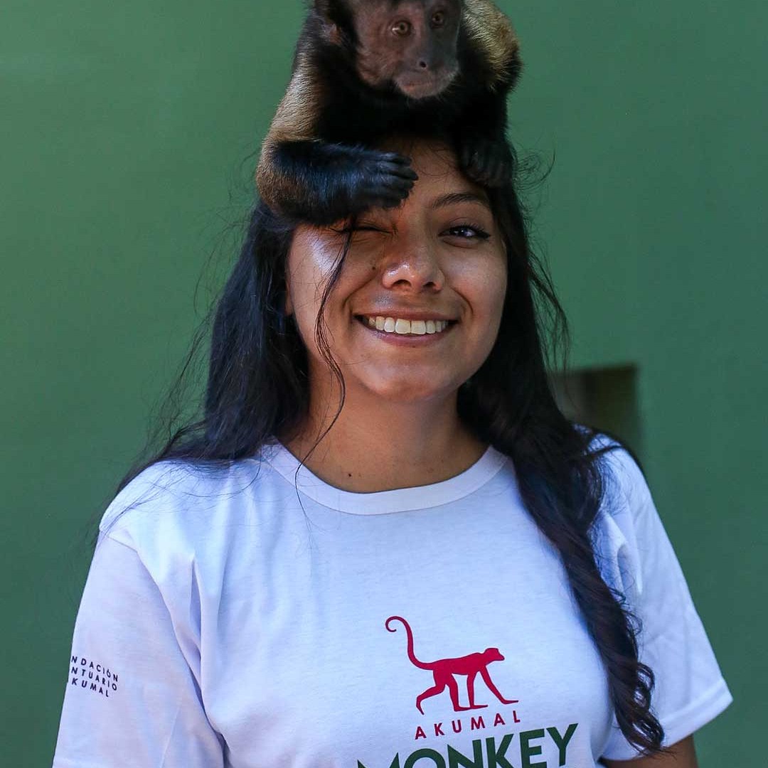 Woman smiling with a monkey on her head, wearing an Akumal Monkey Sanctuary T-shirt.