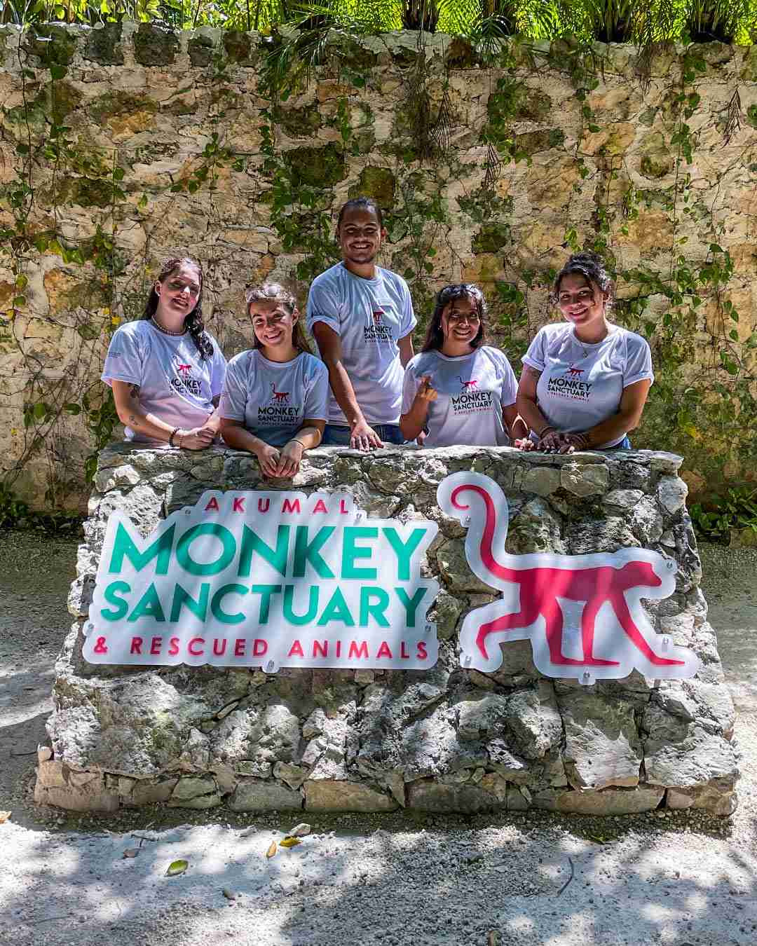 Five people stand behind a sign for Akumal Monkey Sanctuary & Rescued Animals.