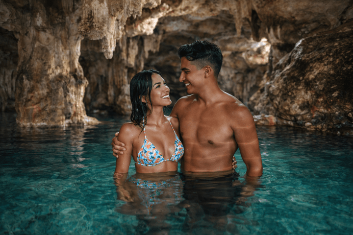 Couple smiling in a water-filled cave with rocky formations.