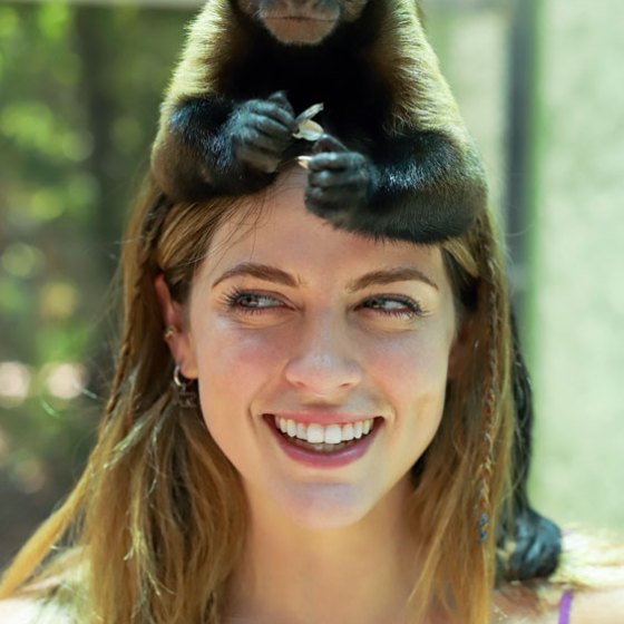 A small monkey sits on a woman's head, both looking forward and smiling.