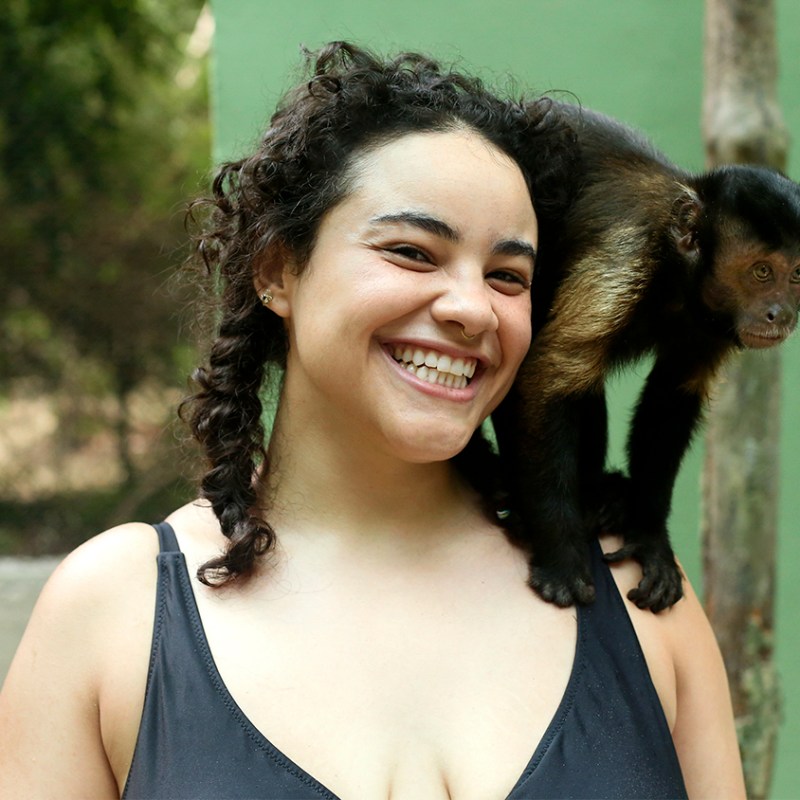 Smiling woman with a monkey on her shoulder outdoors.